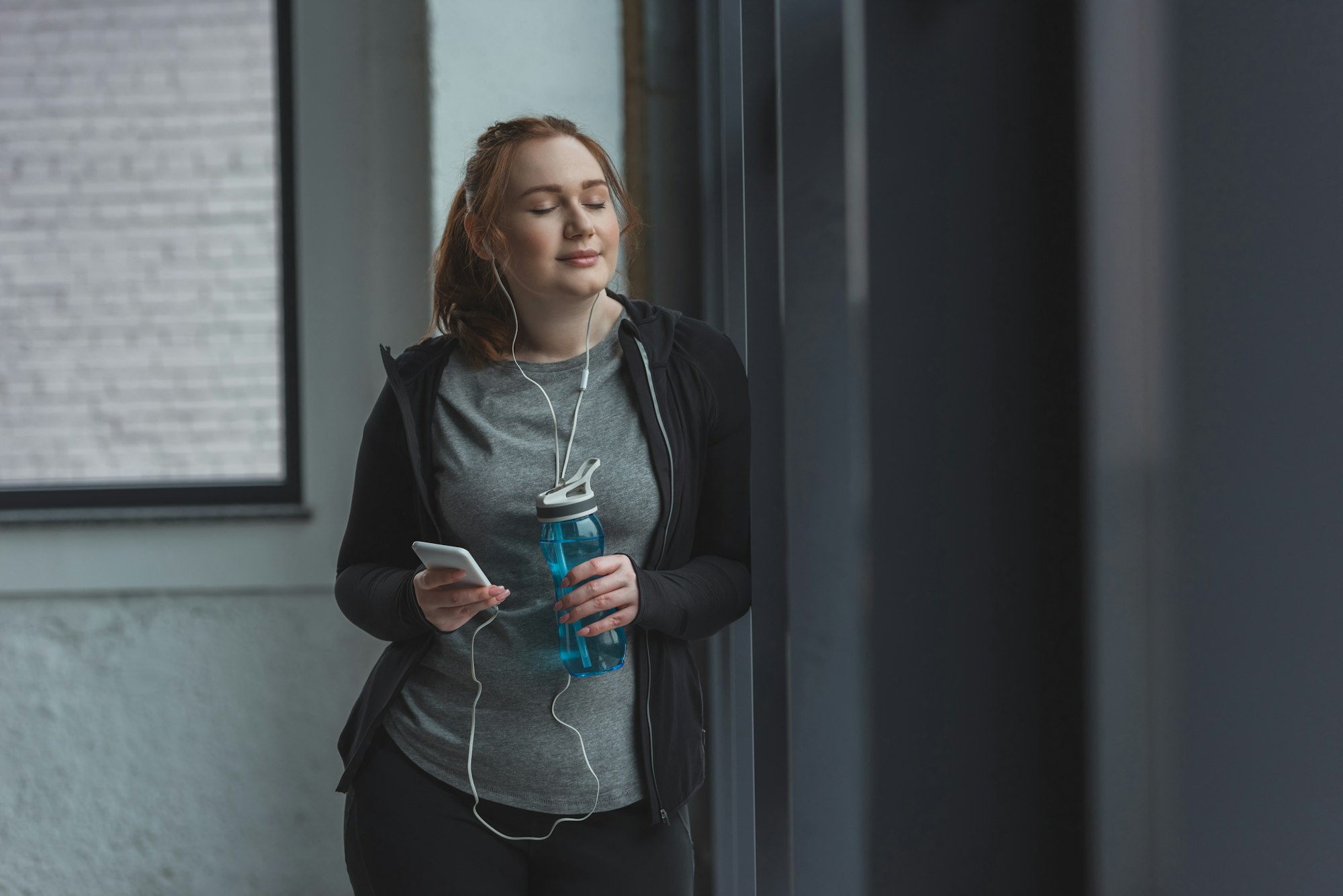 Obese girl with water bottle listening to music in gym